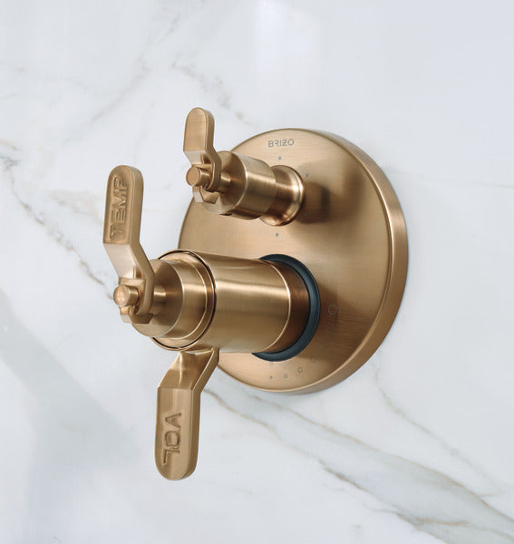 Luxe gold thermostatic valve trim with dual lever handles and circular escutcheon plate mounted on marble surface.