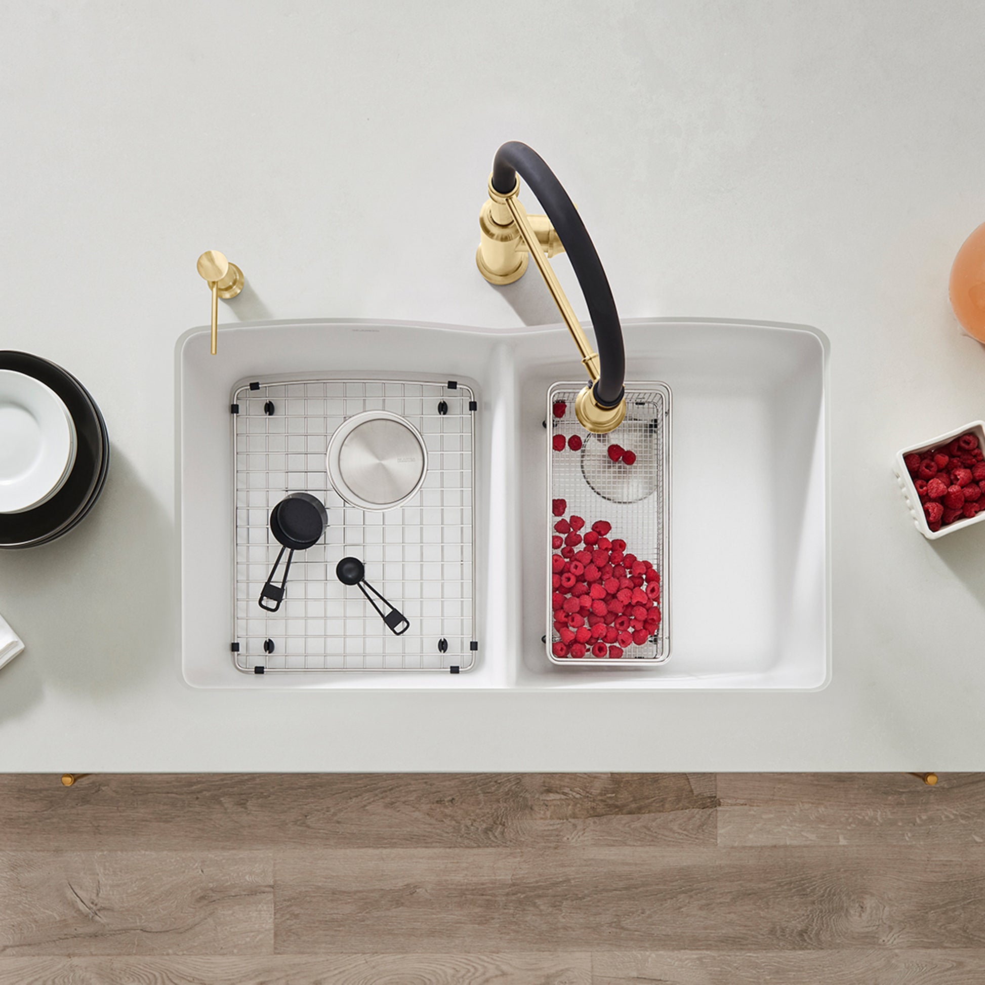 White undermount double bowl kitchen sink with equal-sized basins, gold faucet with black handle, and grid inserts installed.