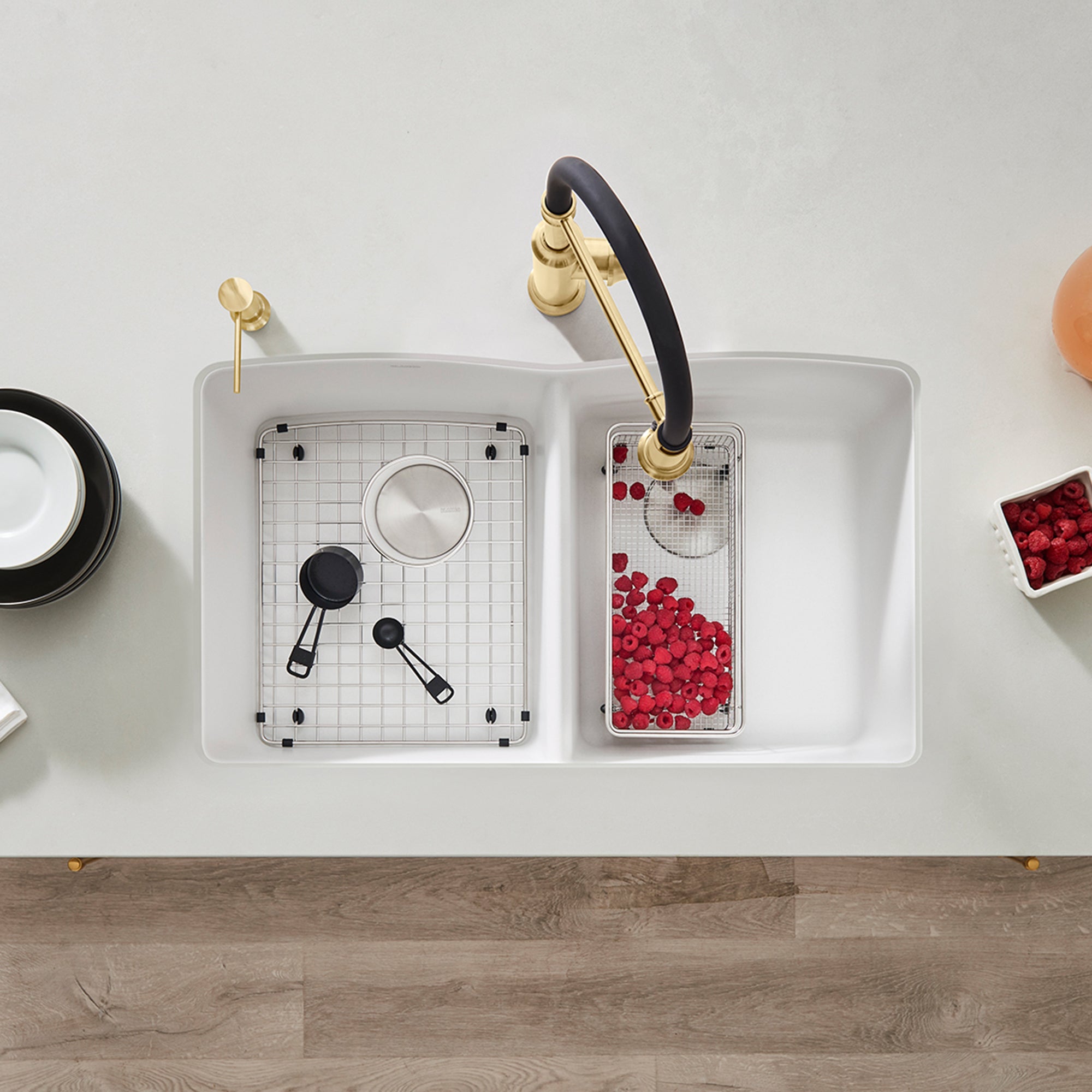 White undermount double bowl kitchen sink with equal-sized basins, gold faucet with black handle, and grid inserts installed.