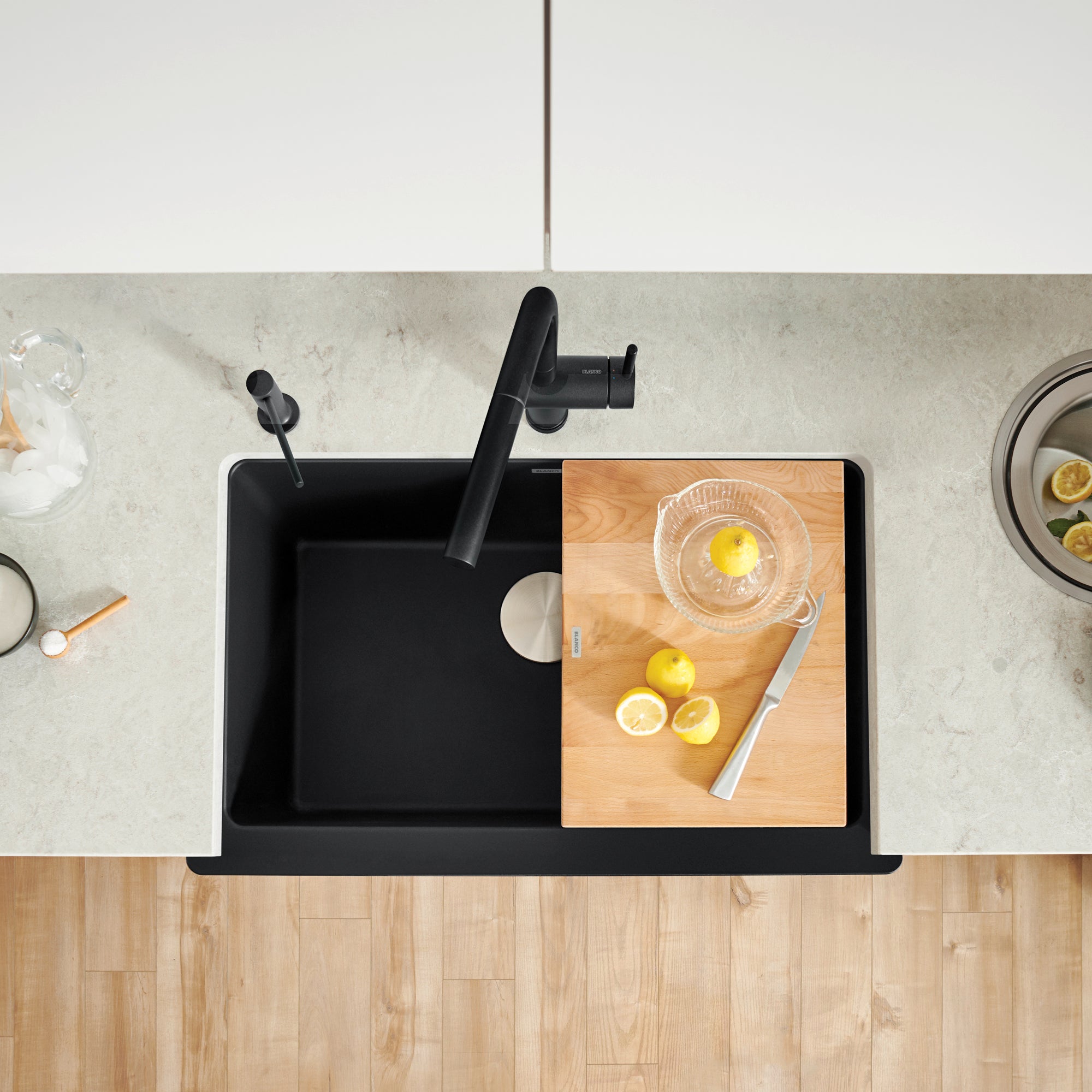 Coal black apron farmhouse sink with single basin, black faucet, and wooden cutting board surface, viewed from above.