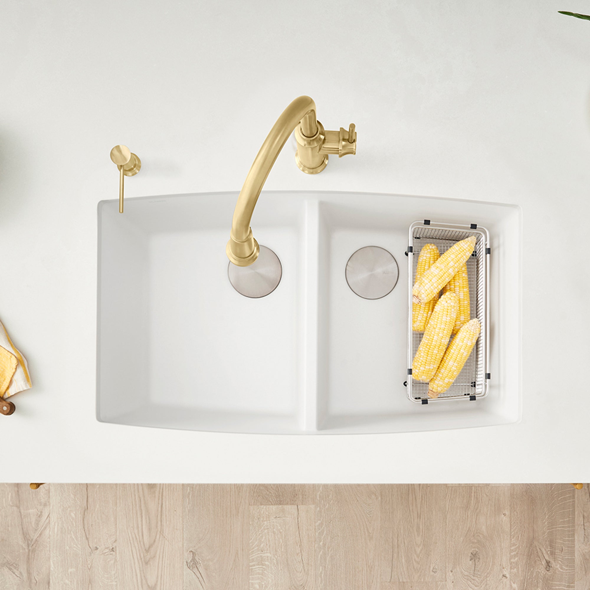 White double-bowl undermount kitchen sink with gold faucet and strainer basket, shown from above.