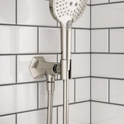 Polished nickel handshower holder with outlet mounted on subway tile wall, featuring round showerhead above.