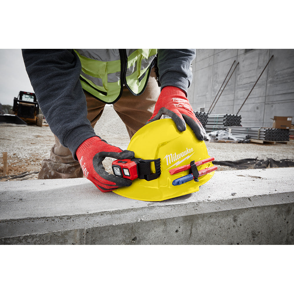 Red hard hat with front brim and vented crown, shown on construction site with ratcheting suspension visible from side.