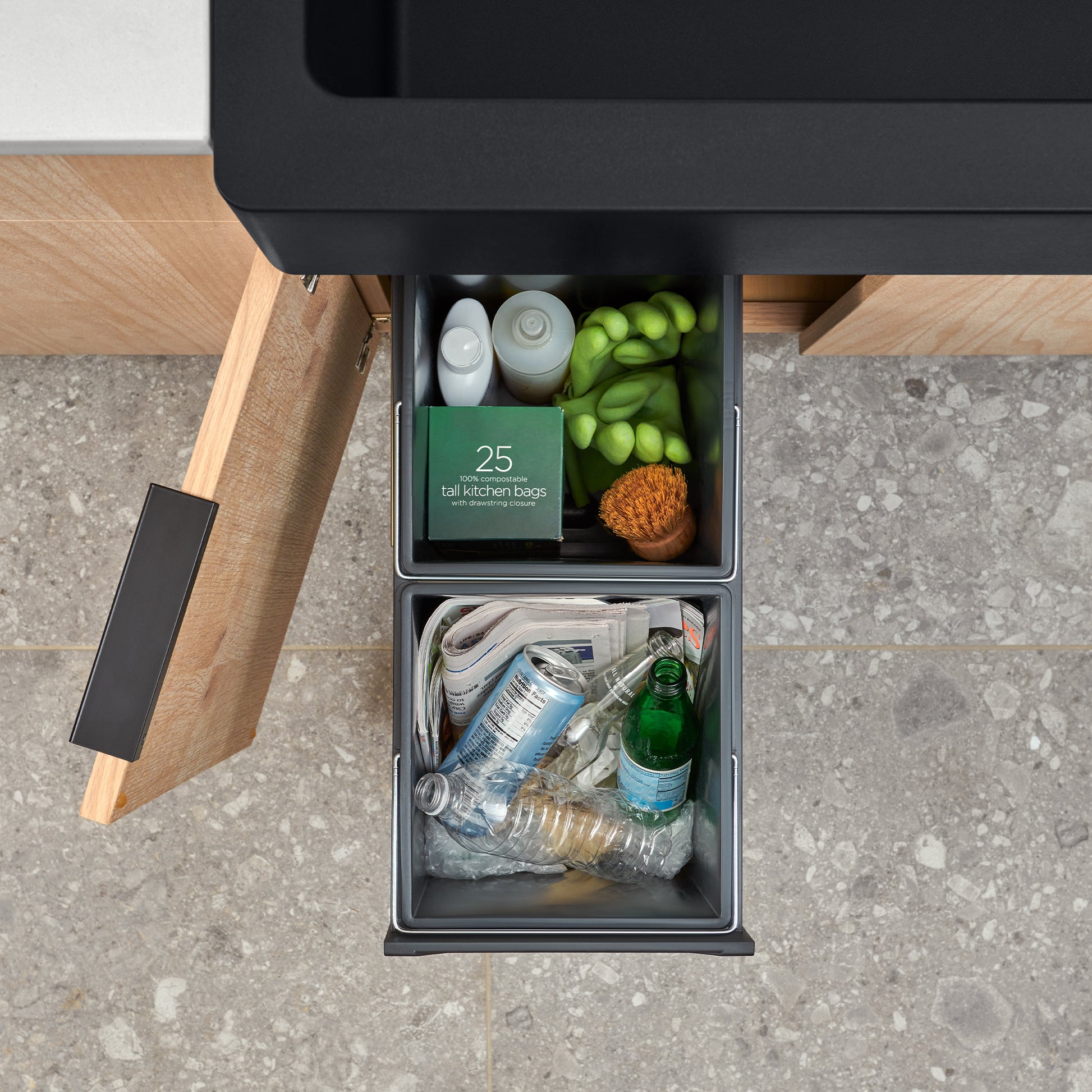 Black pull-out storage drawer system with two compartments holding kitchen items, produce, and recyclables.