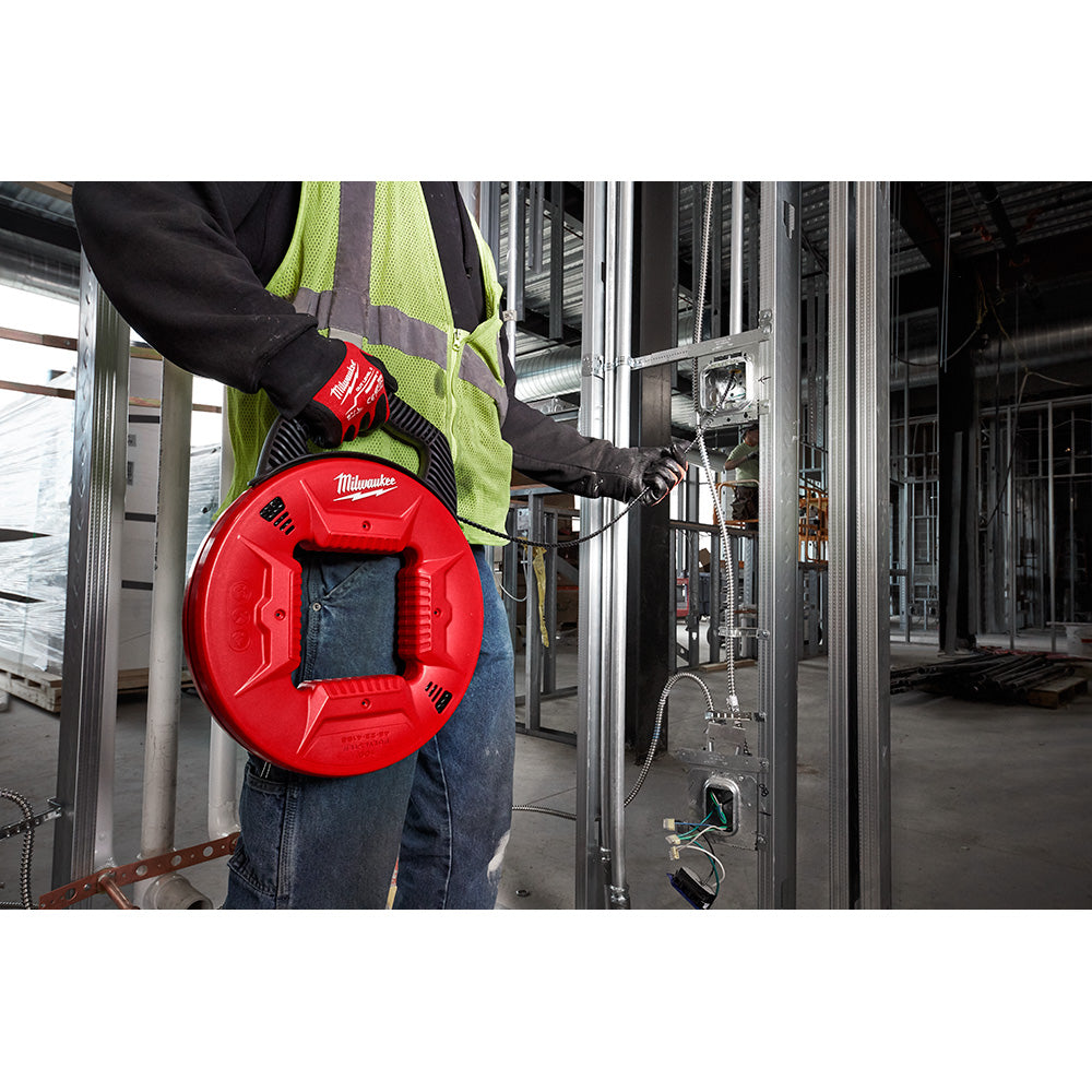 Red circular fish tape reel with black handle held by worker in safety vest during electrical conduit installation.
