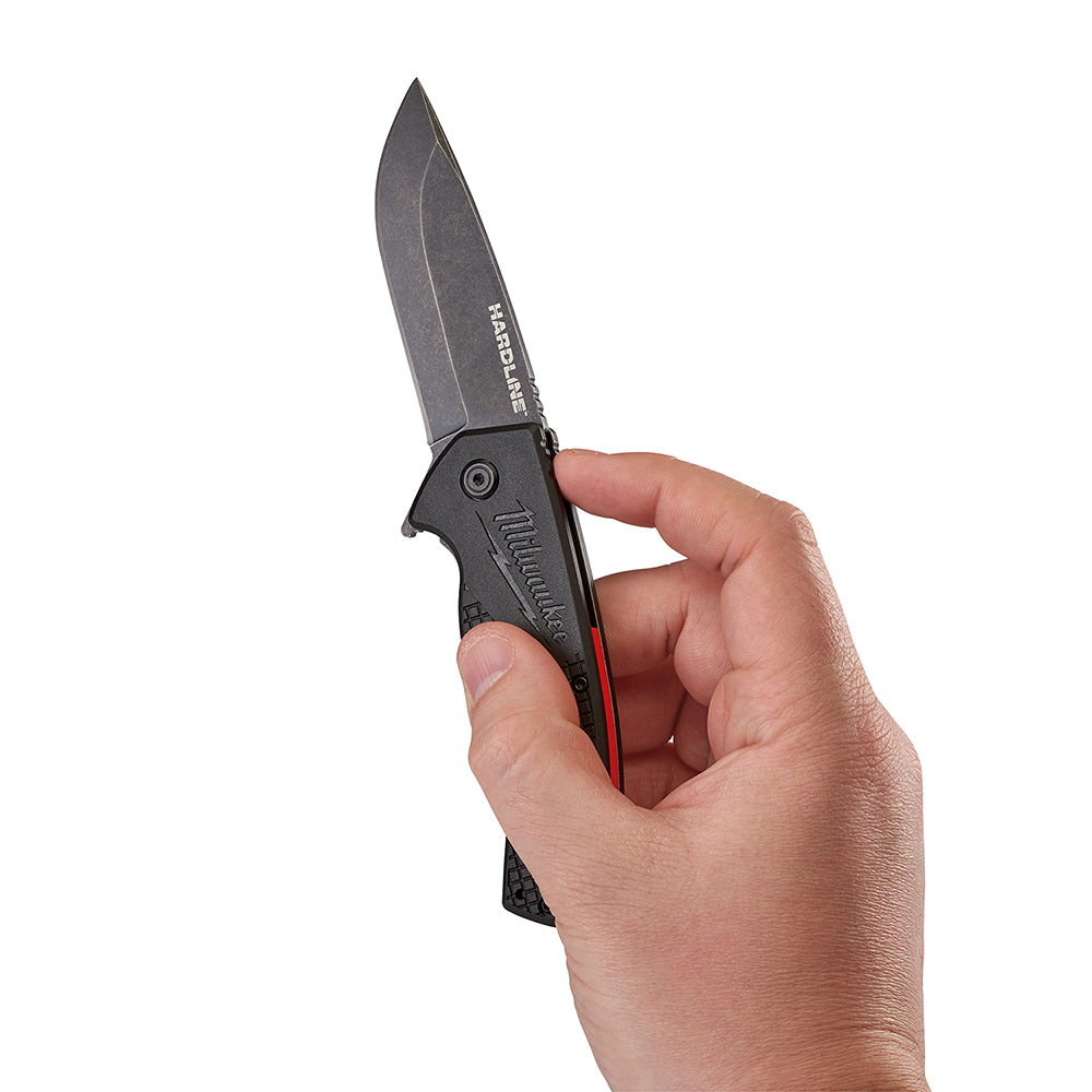 Black pocket knife with smooth blade held open in hand, showing gray blade and black handle with red accent strip.