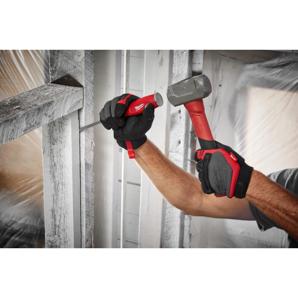 Red and black demolition driver hammer with padded grip held in gloved hands against wooden framing.