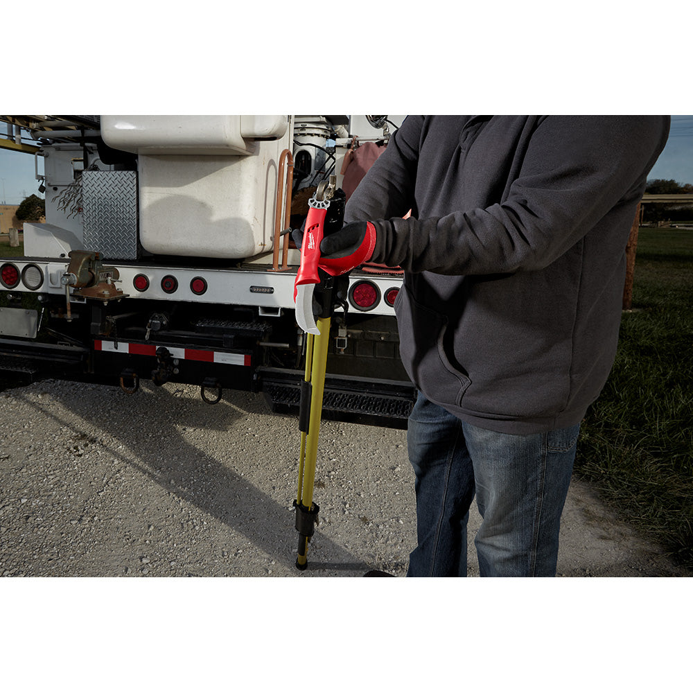 Person in black jacket holding lineman's hawkbill knife with red ring attachment near utility truck.