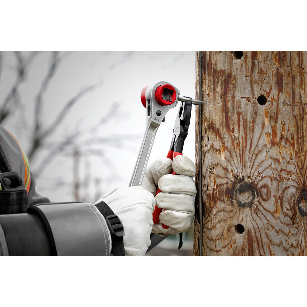Milwaukee ratcheting wrench with red and silver head held in gloved hand against wooden surface.