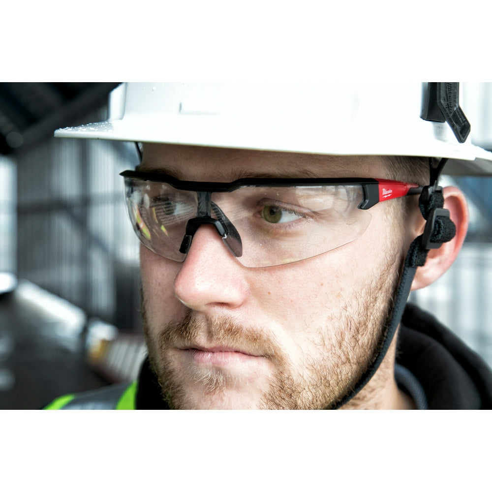 Clear safety glasses with black frames worn over a hard hat on a construction worker's face.