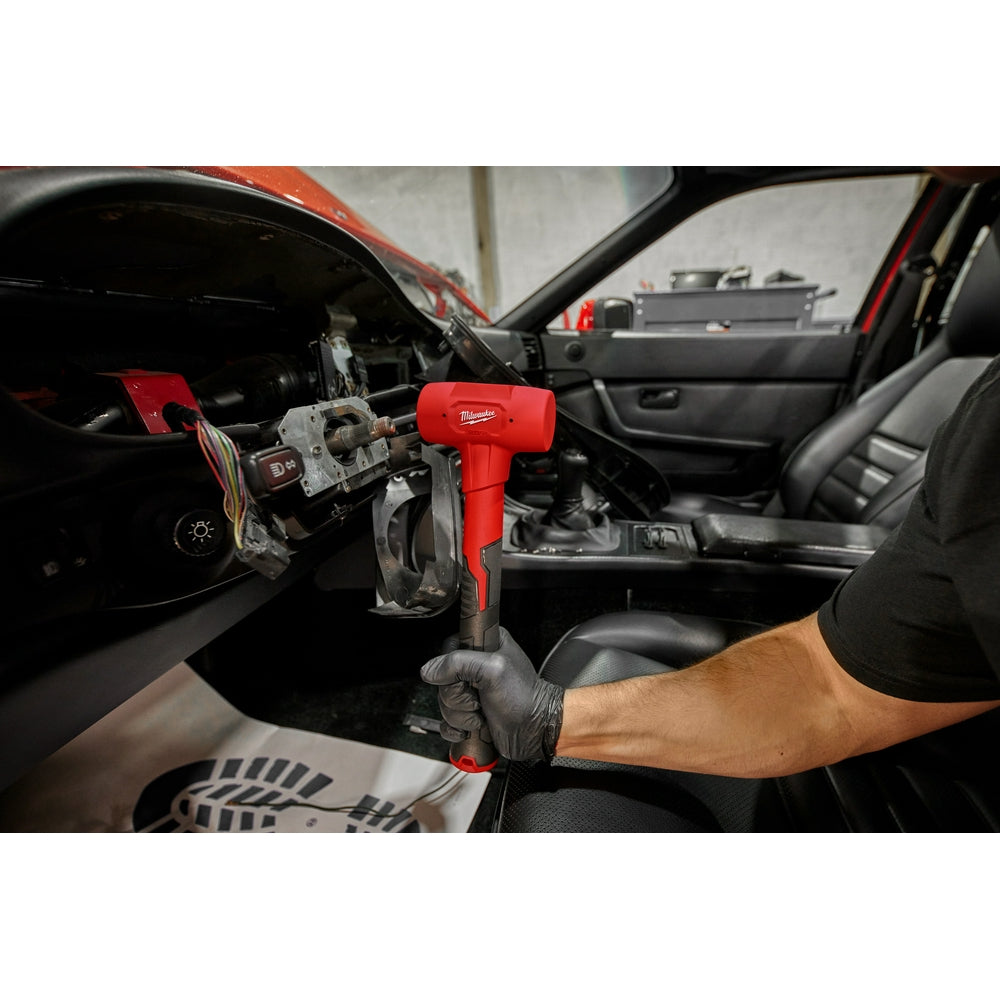 Red and black Milwaukee dead blow hammer with cushioned head, held in a gloved hand above a car interior.