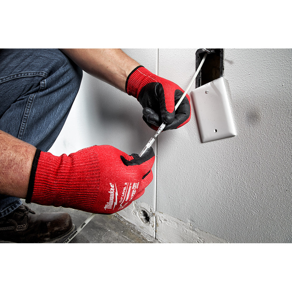Person wearing red and black gloves using a flexible fish stick to thread wire through wall outlet opening.