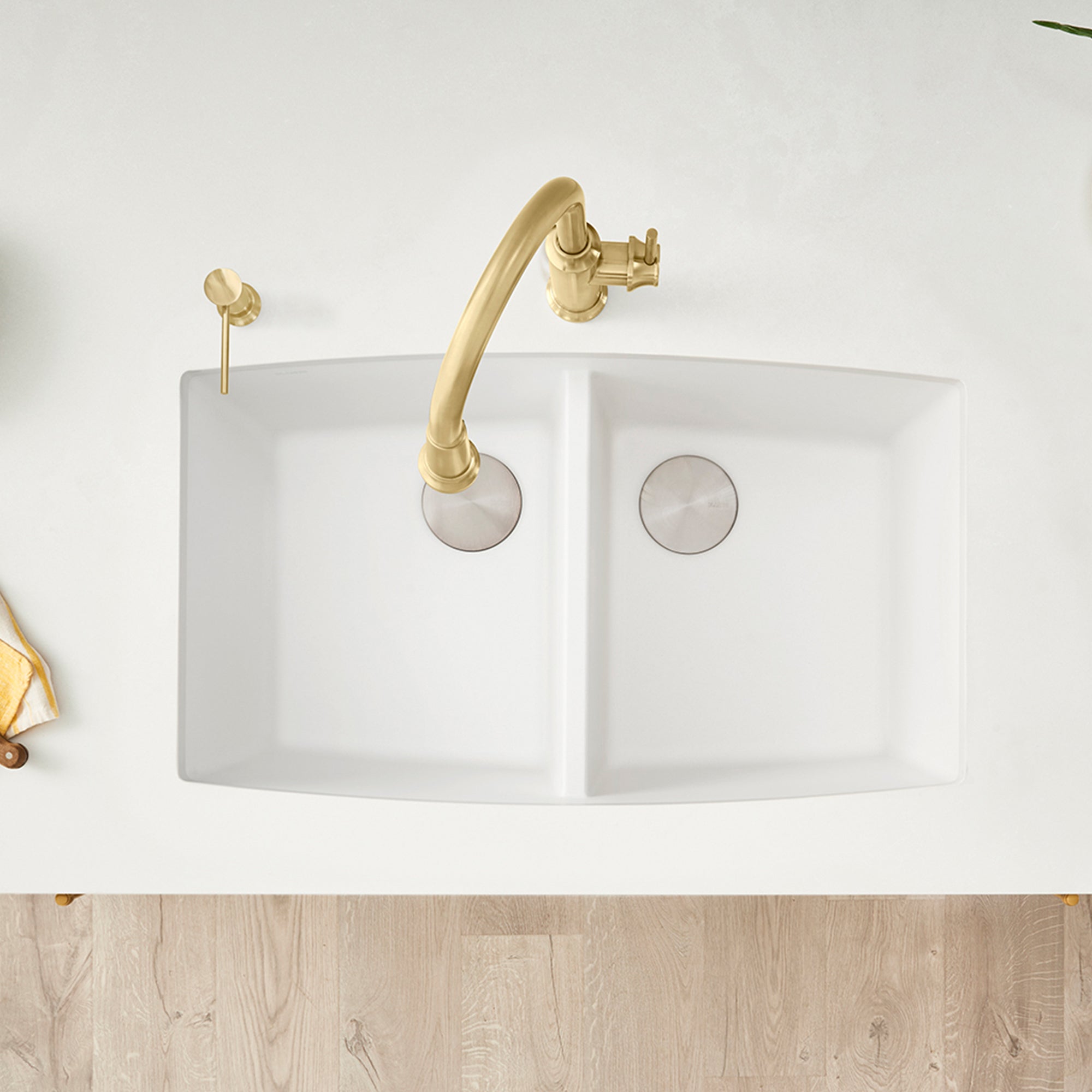 White double bowl undermount kitchen sink with brass faucet and strainer, viewed from above.