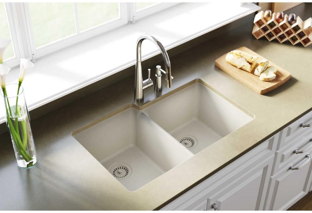 Bisque quartz double bowl undermount sink installed in light countertop with chrome faucet and drain strainers visible.