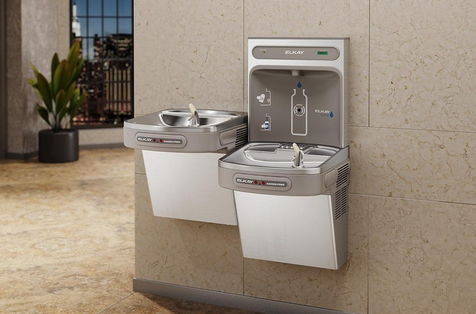 Stainless steel and white Elkay bi-level water filling station with dual fountains and wall-mounted cooler unit in institutio
