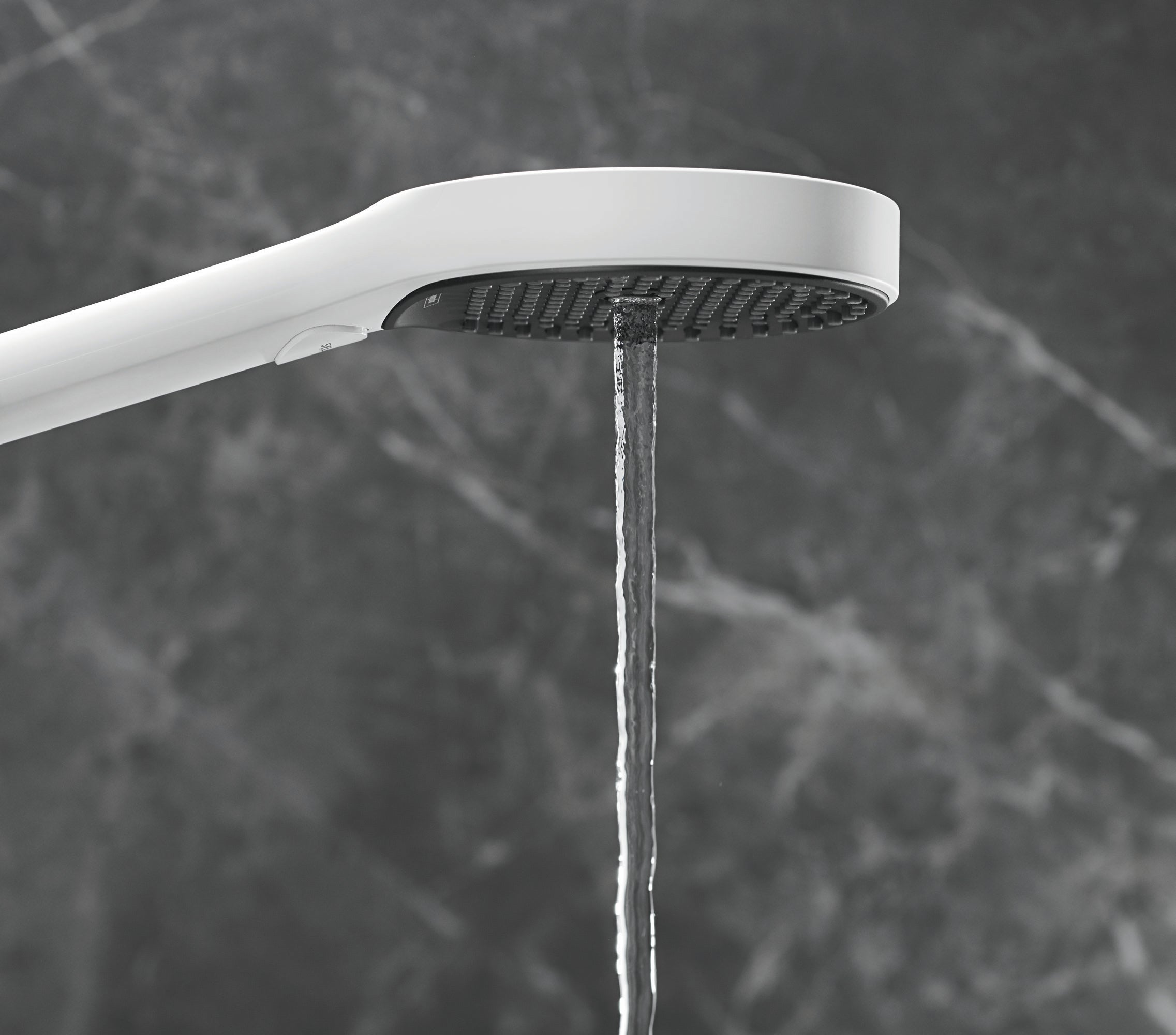Matte white handheld showerhead with circular perforated face and curved arm, water stream visible below.