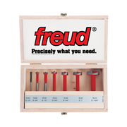 Seven Freud Forstner bits with red handles and gray cutting heads in wooden storage case with labeled compartments.