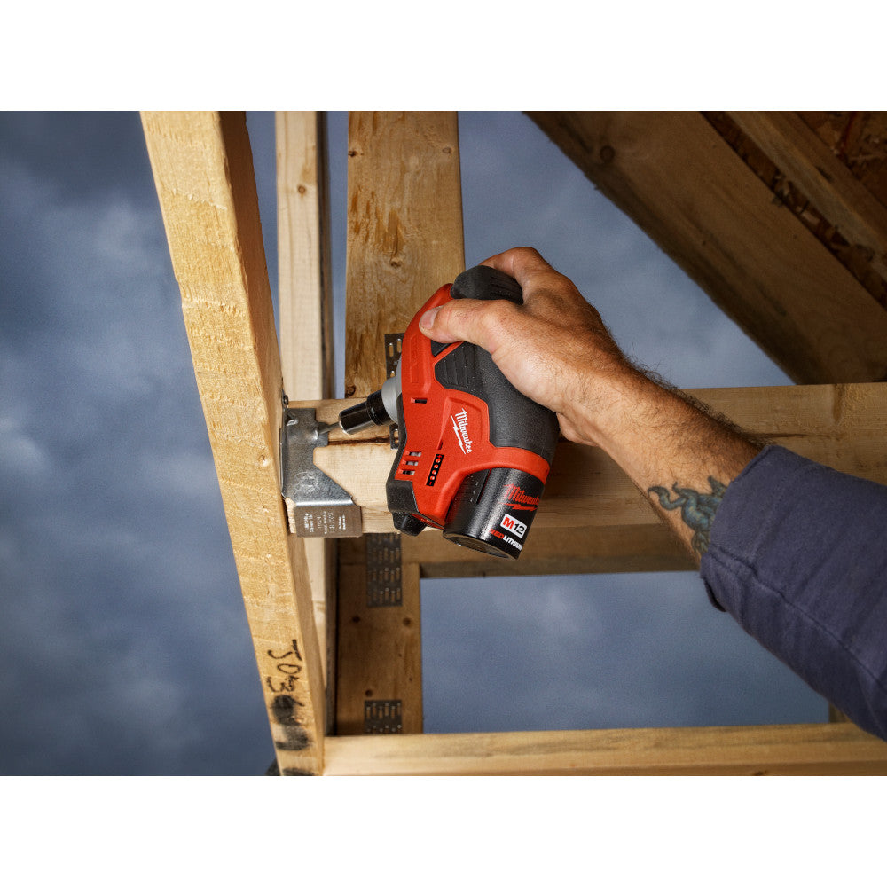 Red and black cordless palm nailer held in hand against wooden framing with nail inserted.