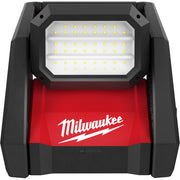 Black and red Milwaukee flood light with grid of yellow LED bulbs on white panel and Milwaukee logo on red base.