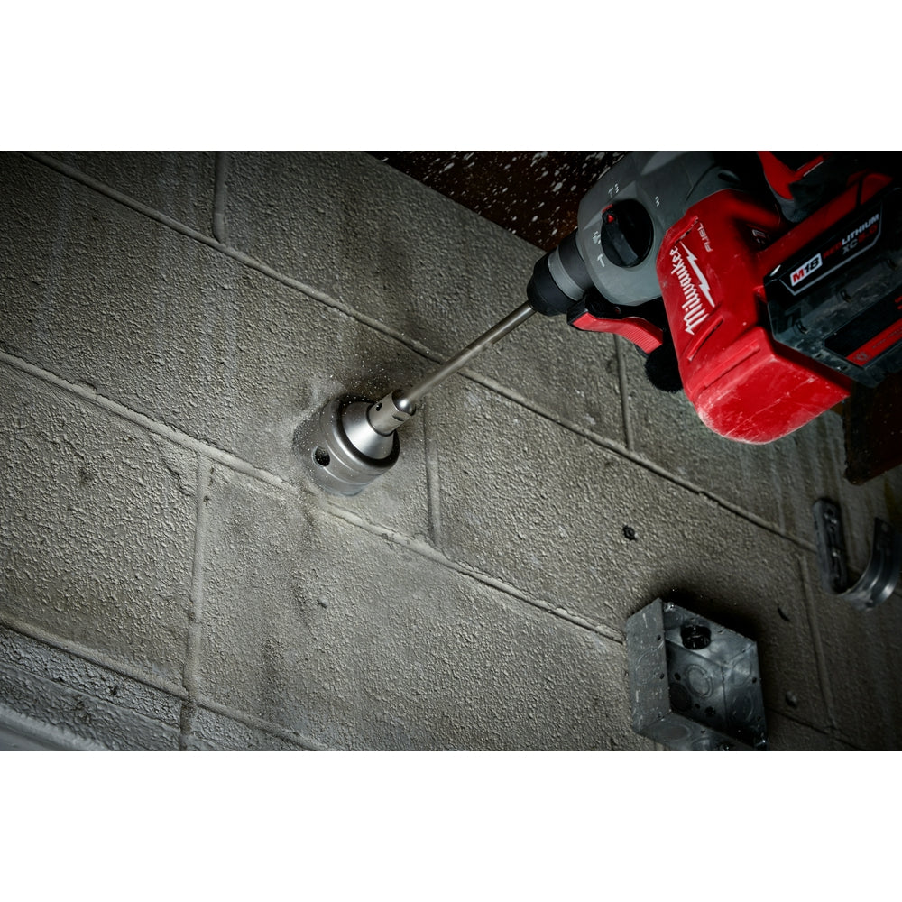SDS+ core bit with carbide tip attached to red Milwaukee drill boring into concrete block wall.