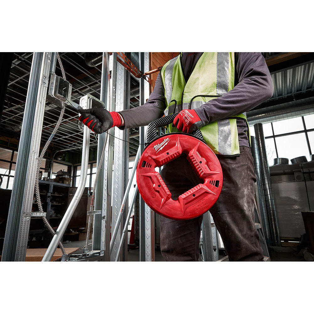 Worker in safety gear holding red Milwaukee fish tape reel with steel tape extended through metal framing.
