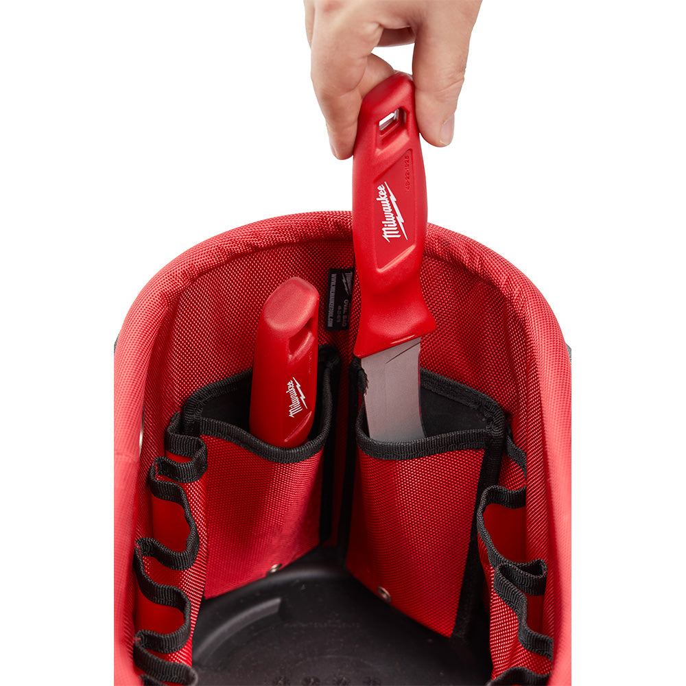 Red Milwaukee Aerial Oval Bag with black handles and interior pockets, held open by hand to show storage compartments.