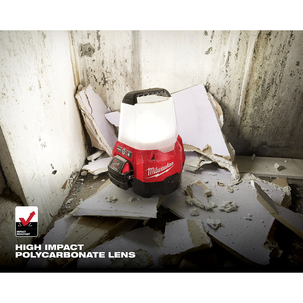 Red and black Milwaukee M18 RADIUS compact site light with white dome lens on concrete surface.