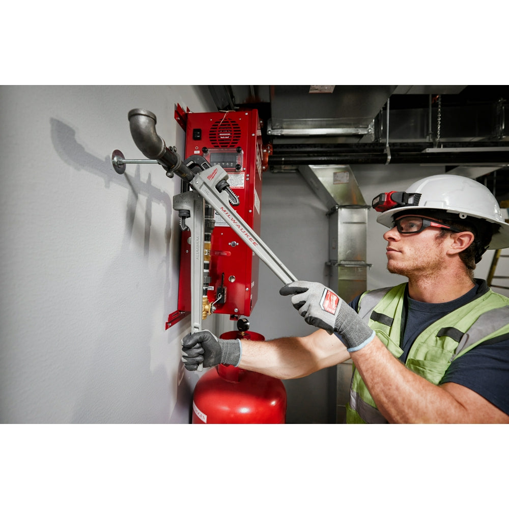 Silver aluminum pipe wrench with adjustable jaw, held by worker in safety gear near red equipment.