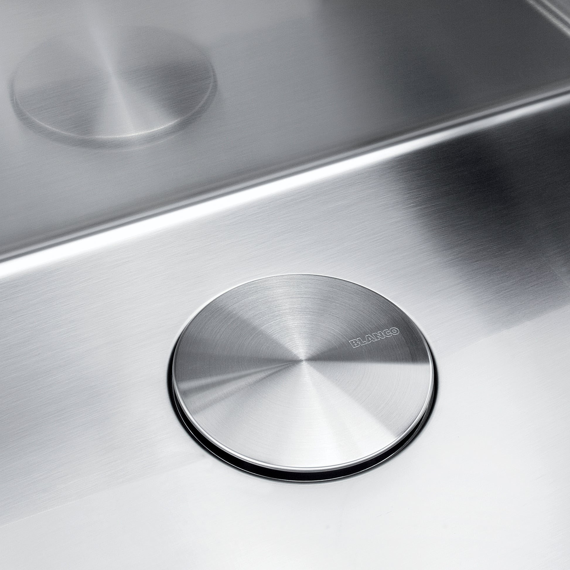 Stainless steel circular drain cover with radial brushed pattern and black rubber rim, installed in sink basin.