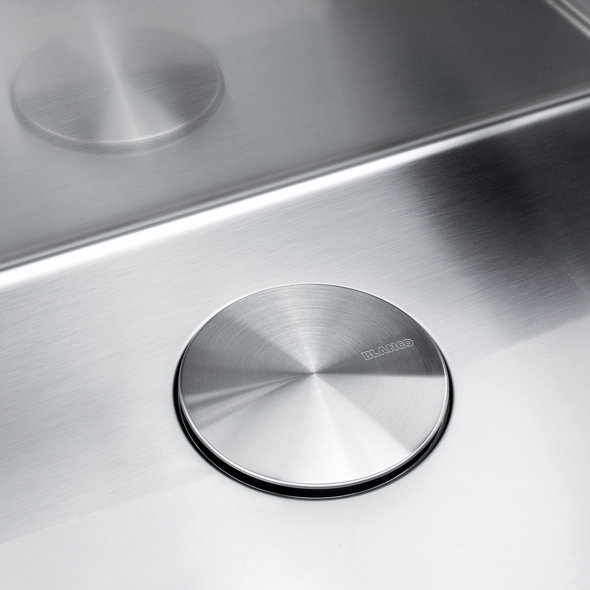 Stainless steel circular drain cover with radial brushed pattern and black rubber rim, installed in sink basin.