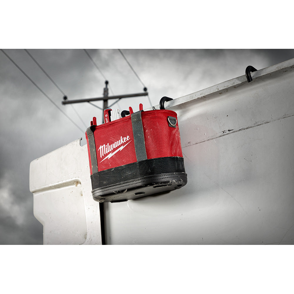 Red and black Milwaukee tool bag with gray straps hanging from aerial ladder on roof.