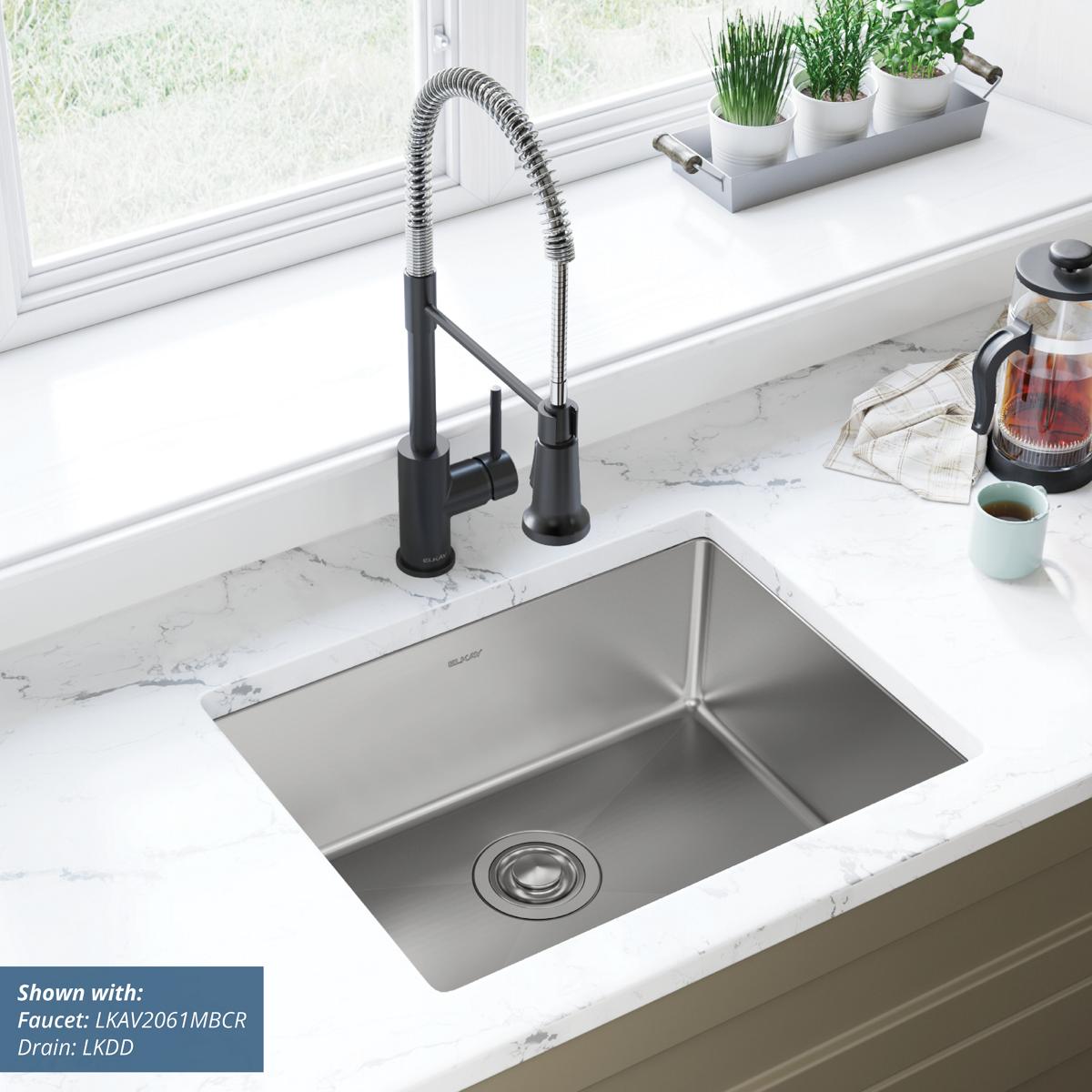 Stainless steel single-bowl undermount sink installed in white marble countertop with black pull-down faucet.