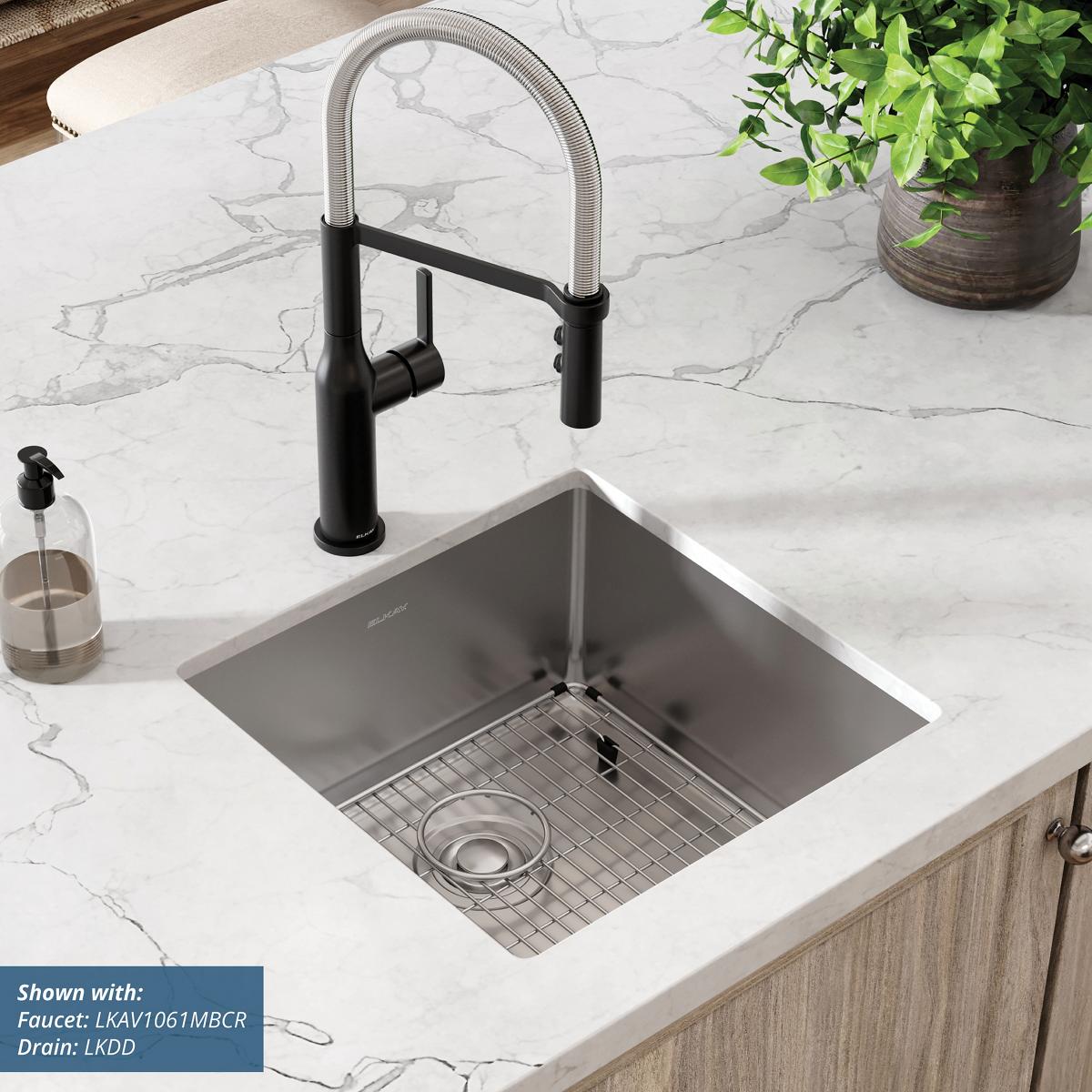 Stainless steel undermount sink bowl installed in marble countertop with black pull-down faucet and grid strainer.