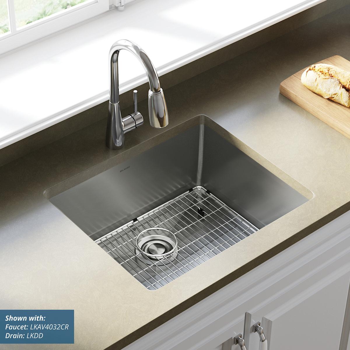 Stainless steel undermount kitchen sink with single bowl, grid, and drain installed in countertop with faucet.