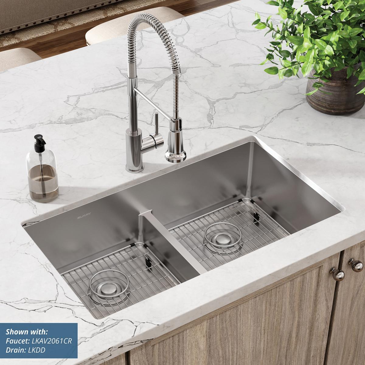 Stainless steel double bowl sink with divider installed in white marble countertop, featuring pull-down faucet and grid strai