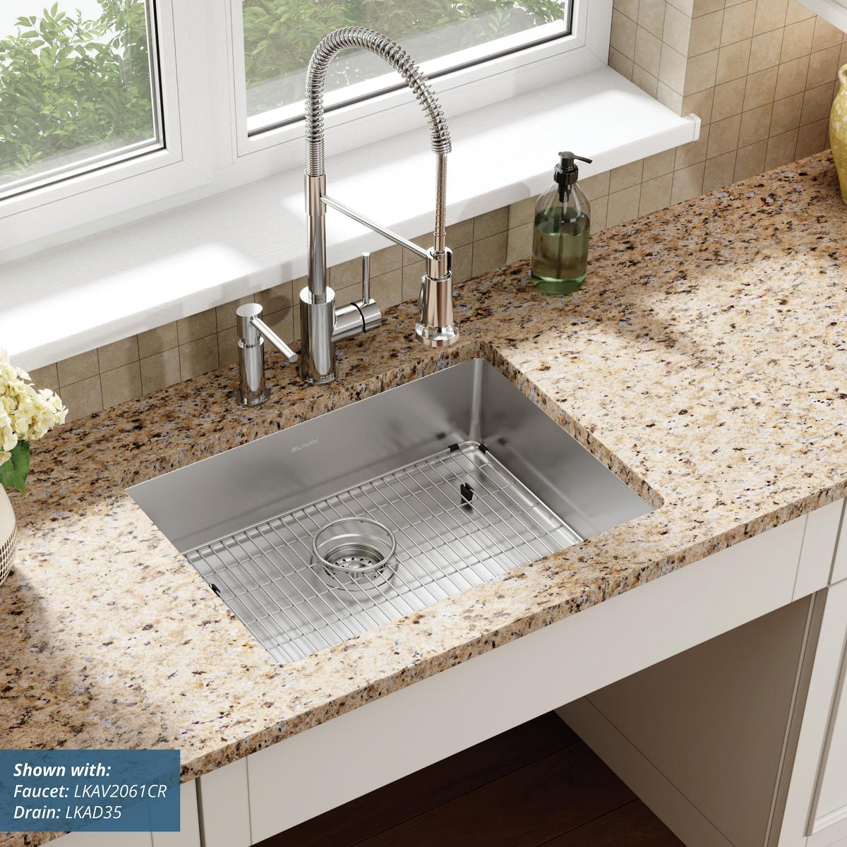 Stainless steel rectangular single bowl sink with two holes, mounted in speckled countertop, includes grid and drain.