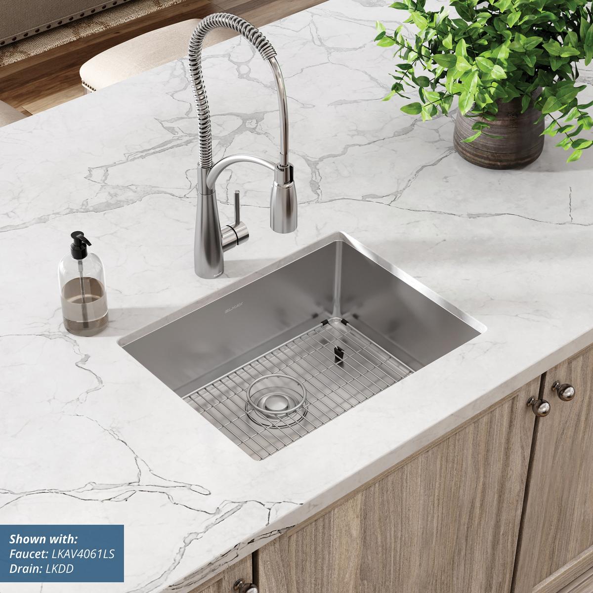 Stainless steel single bowl undermount sink installed in marble countertop with faucet and grid strainer.