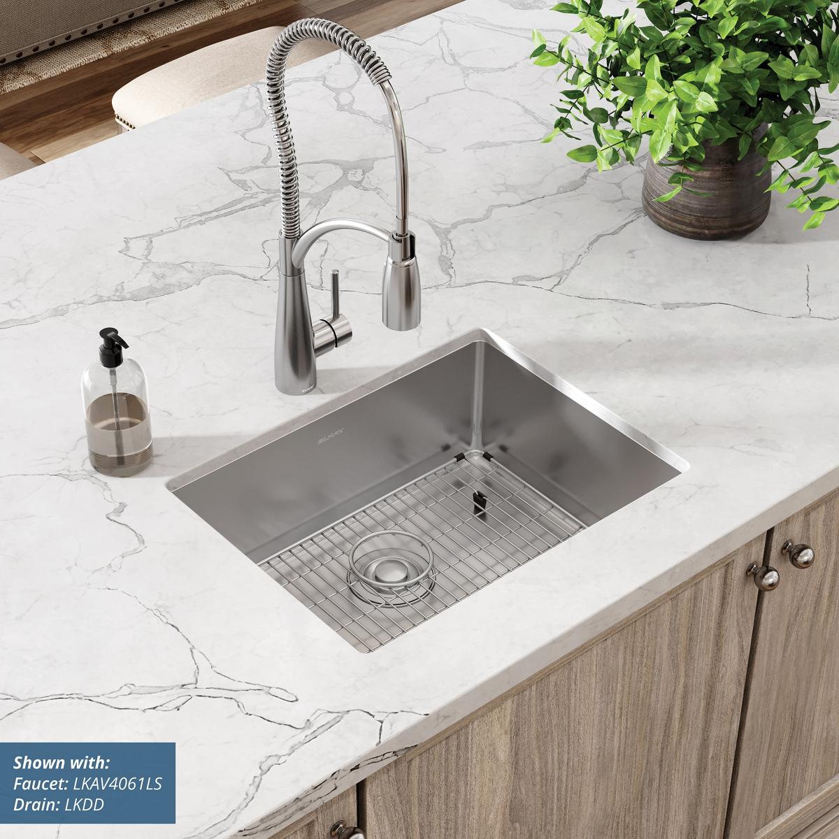 Stainless steel undermount sink with single bowl, grid insert, and pull-down spray faucet on marble countertop.