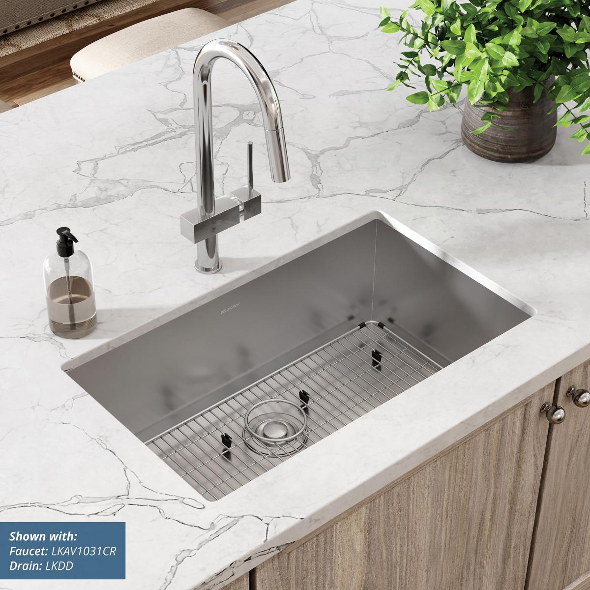 Stainless steel undermount sink with rounded corners, grid insert, and chrome faucet installed in white marble countertop.