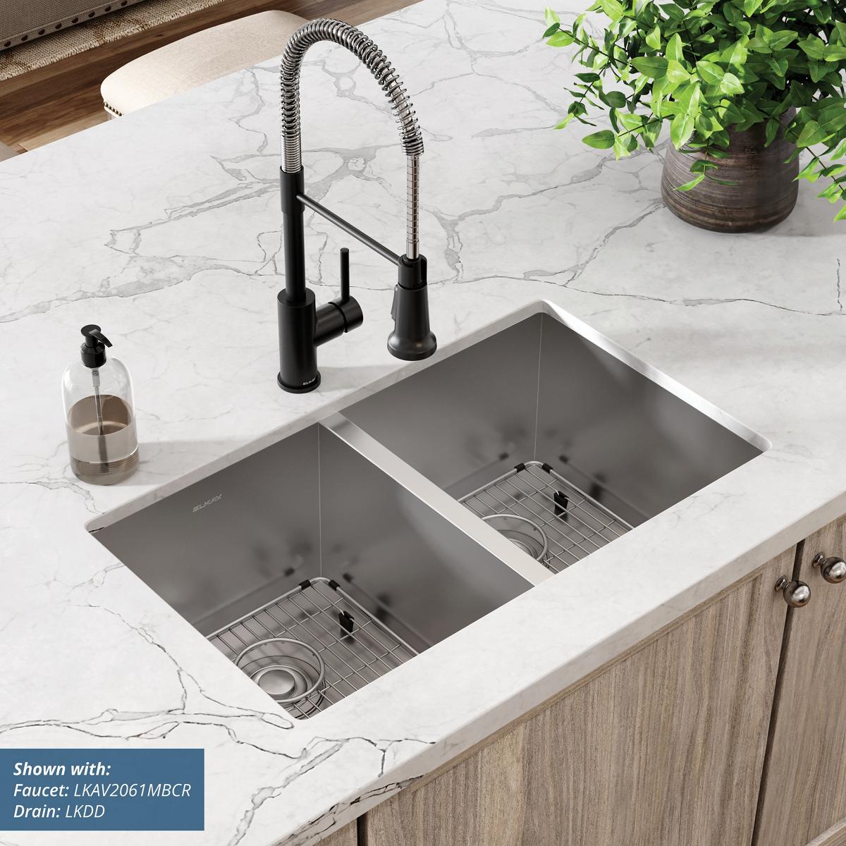 Stainless steel double bowl undermount sink installed in white marble countertop with black pull-down faucet and drain grids.
