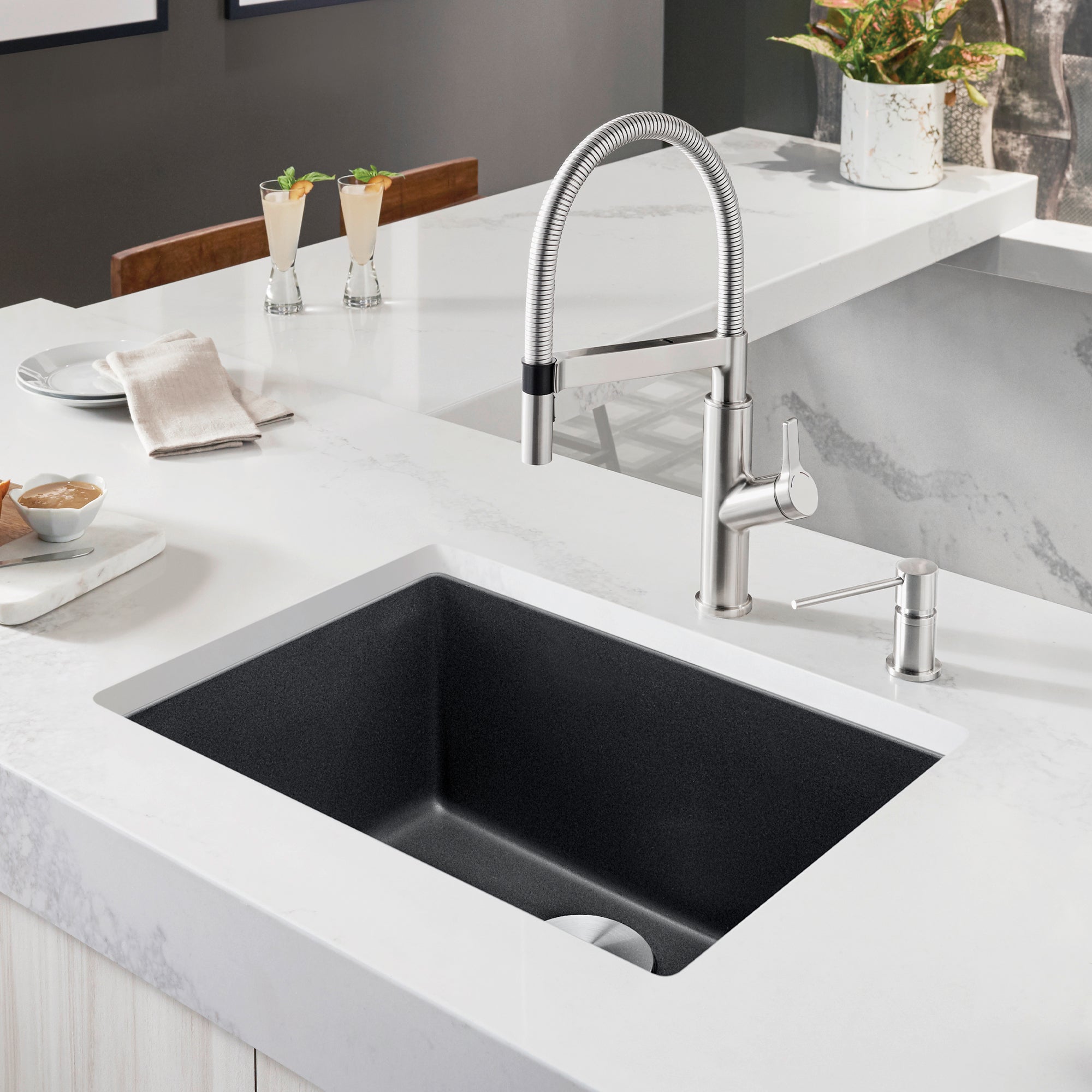 Anthracite single bowl undermount sink with chrome pull-down faucet and spray head installed in white countertop.