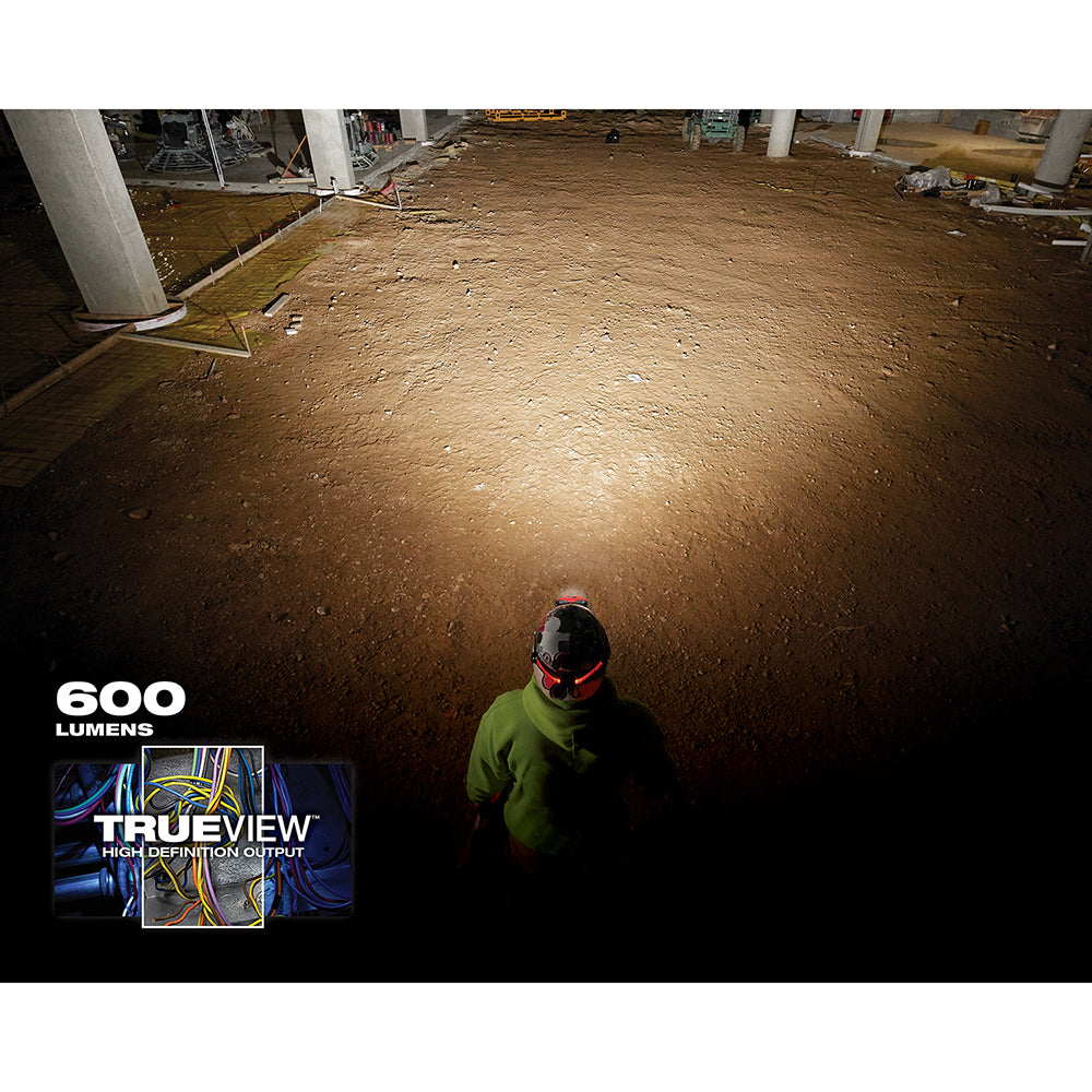Worker wearing red and black hard hat with light attachment illuminating construction site floor.