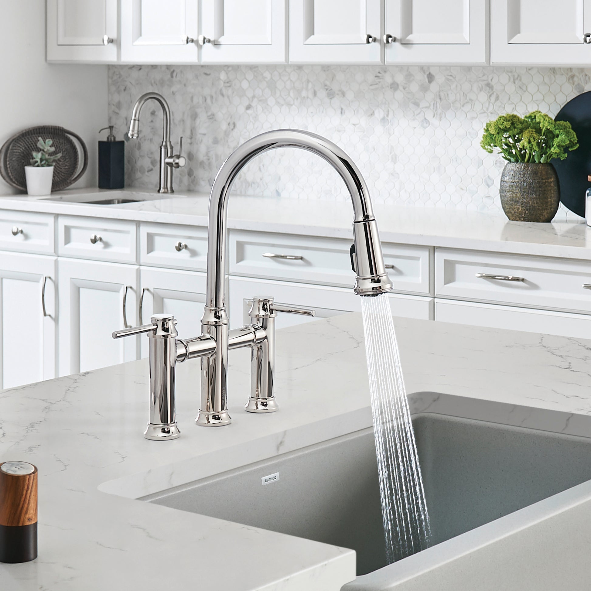 Chrome bridge kitchen faucet with arched pull-down spout and dual handles installed above undermount sink.