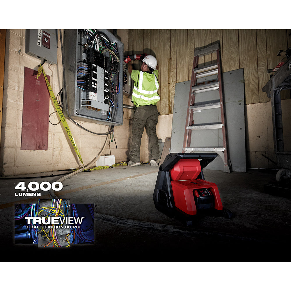 Red and black Milwaukee M18 flood light positioned on concrete floor in construction setting, illuminating work area.