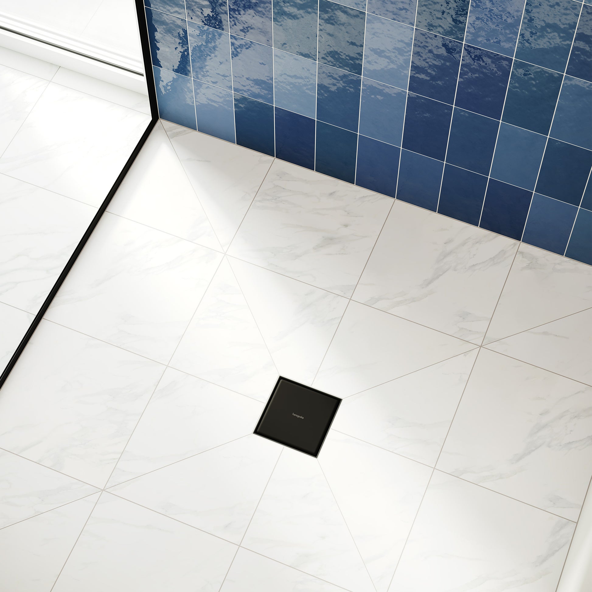 Square matte black shower drain installed in marble tile floor with blue tile wall visible in background.