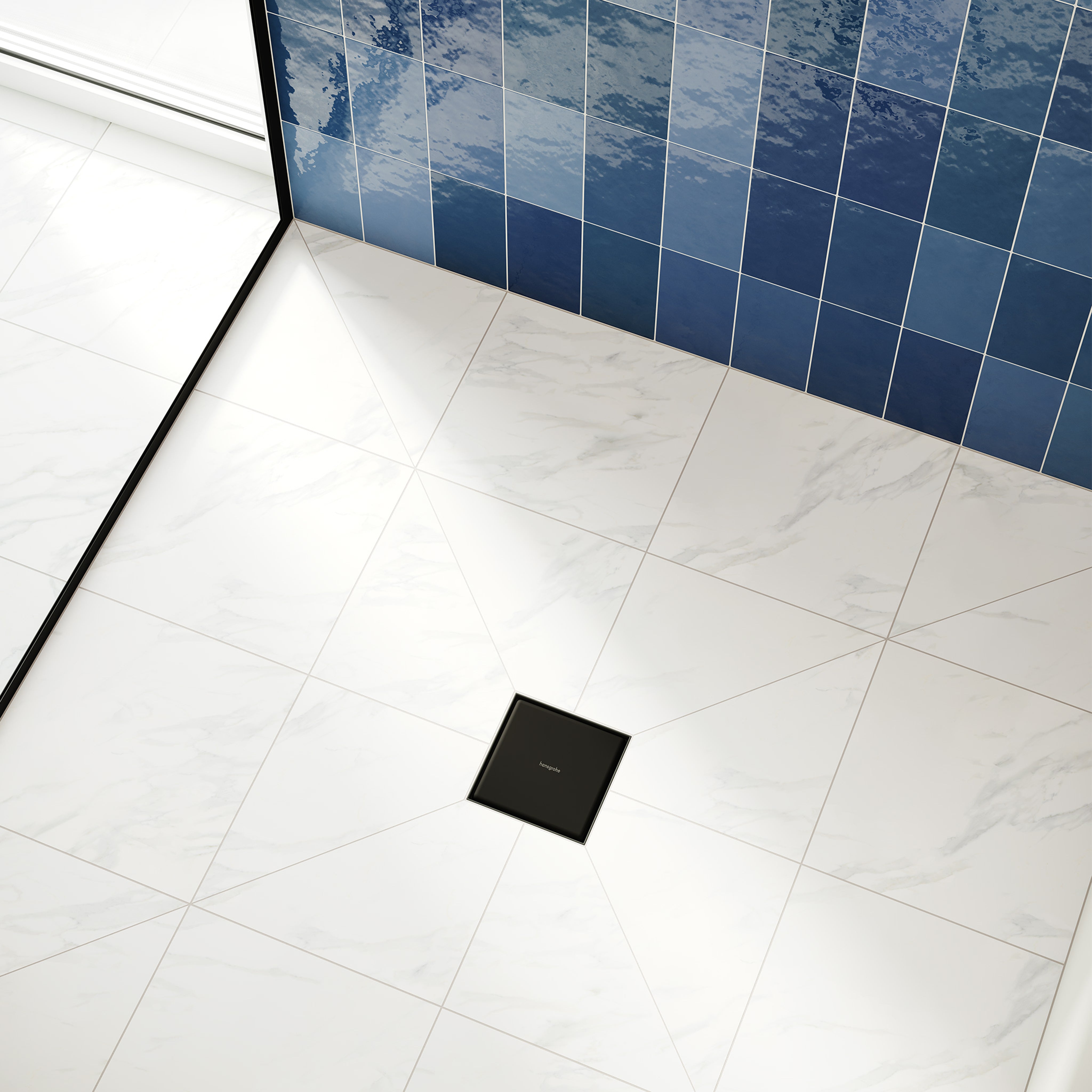 Square matte black shower drain installed in marble tile floor with blue tile wall visible in background.