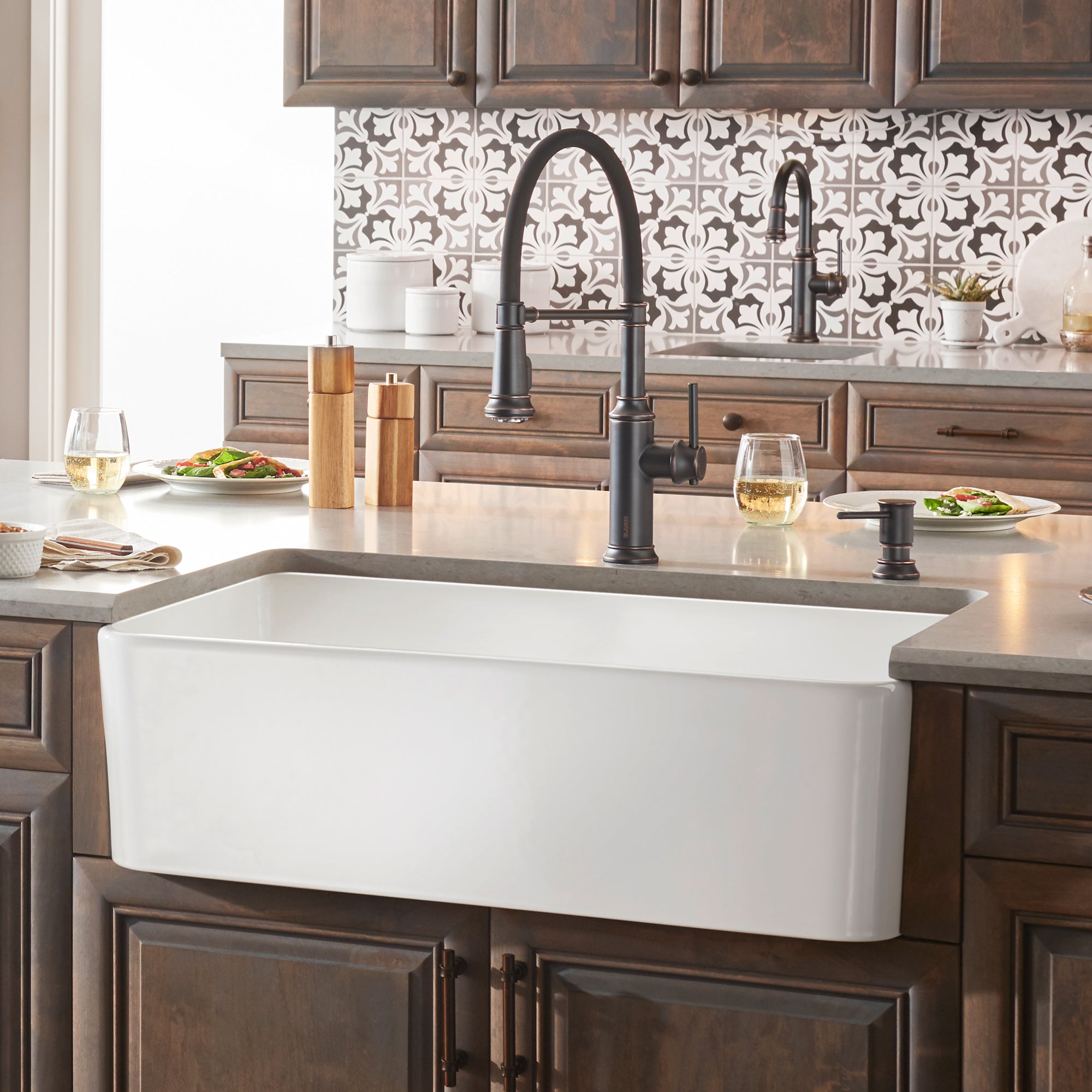 White single-bowl farmhouse sink with apron front installed in kitchen counter with black faucet and wooden cabinetry.