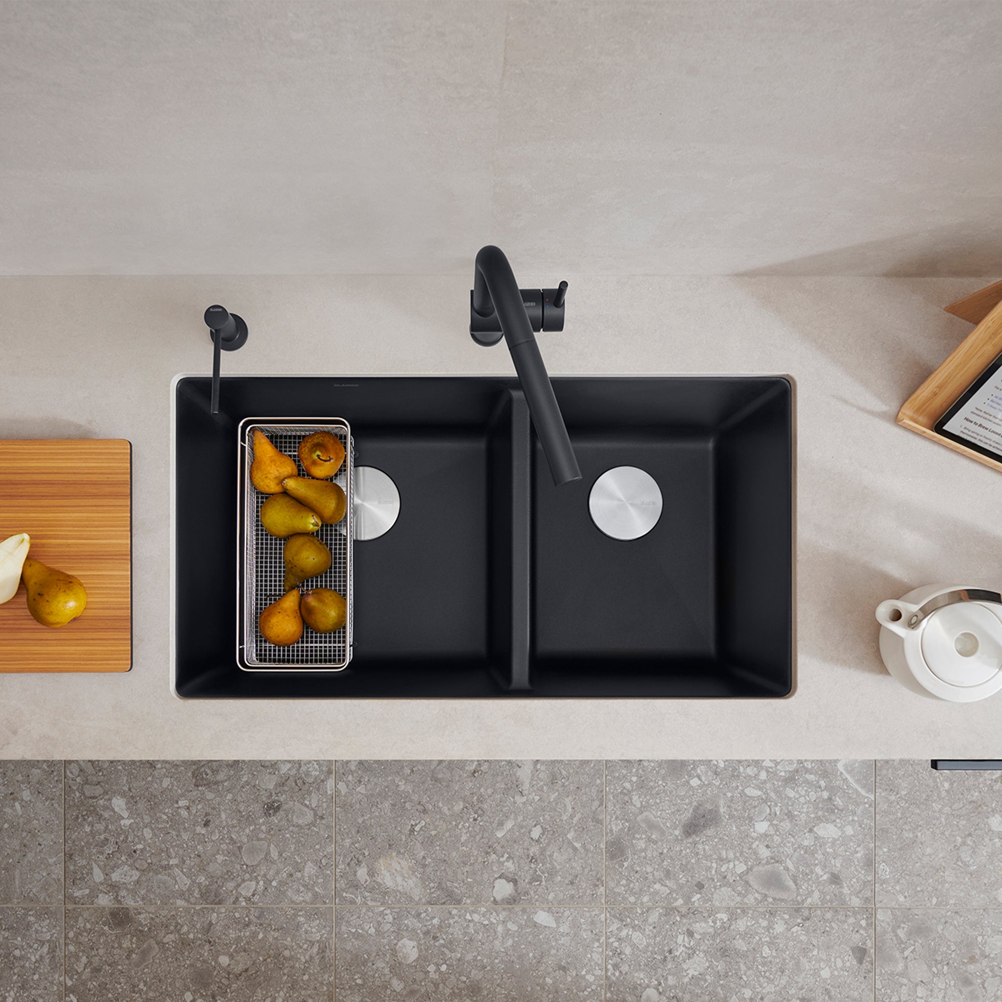 Coal black double bowl undermount kitchen sink with left bowl containing strainer basket and produce, right bowl empty, black