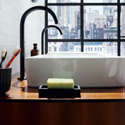 Black circular soap dish holding a green bar of soap on a bathroom counter.