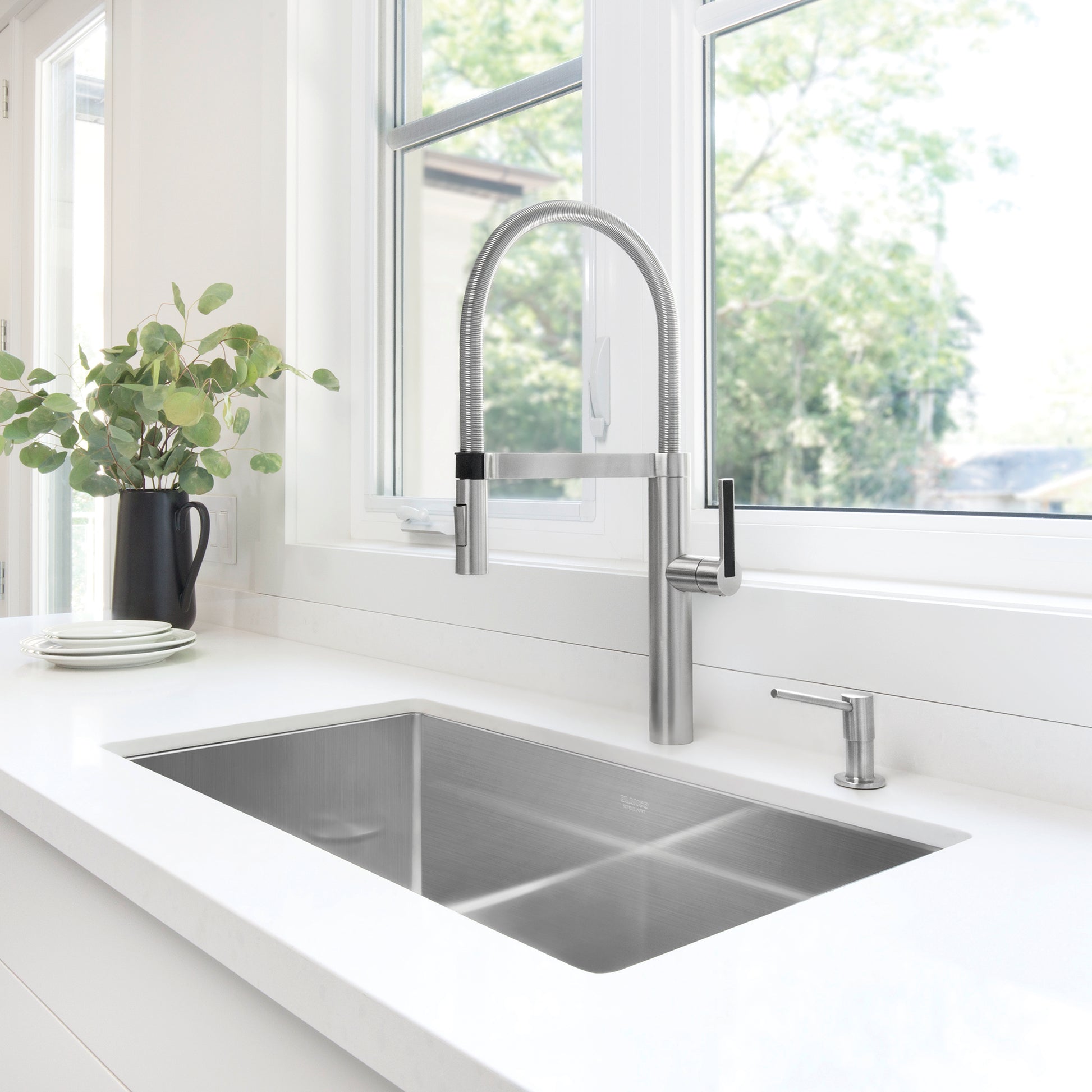 Stainless steel undermount kitchen sink with single bowl and matching faucet installed in white countertop.